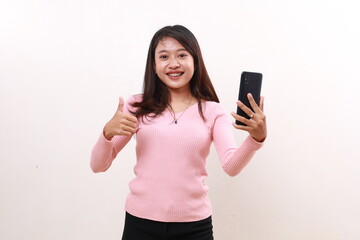 Fototapeta premium Happy young asian woman showing a thumbs up while holding a cell phone. Isolated on white