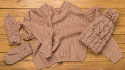 Sweater and winter hat with mittens on wooden background, top view.