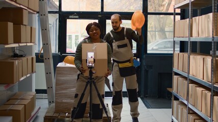 Warehouse marketing expert using smartphone placed on tripod to make ad campaign for social media...