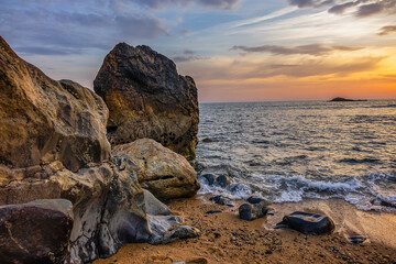 Landscape of the picturesque sandy coast of the Atlantic Ocean with large brown stones at sunset....