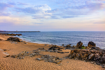 Landscape of the picturesque sandy coast of the Atlantic Ocean with large brown stones at sunset. Porto, Portugal.