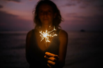 woman holding sparkles celebrating on tropical beach - obrazy, fototapety, plakaty