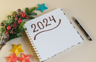 Obraz na płótnie Canvas Notepad with 2024 lettering, pen and decorations rests on a light background. For cards, social posts, and banners.