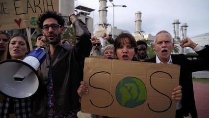 Group of people at a refinery protesting against global warming. Crowd demonstrating for problems in ecology, environment, climate change, industrial influence, climate emergency.