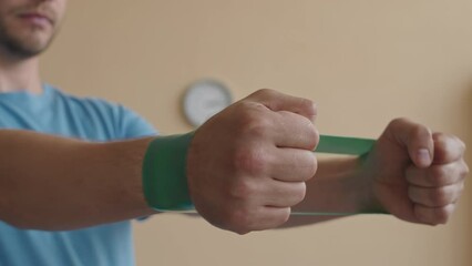 Close up shot of hands of male patient pulling resistance band while doing rehabilitation exercise under control of female doctor in physiotherapy clinic