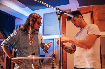 Music producer talking to a drummer next to a drum set.