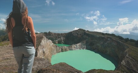 Naklejka premium Tourist woman enjoy morning view on volcanic Kelimutu blue crater lakes. Nature background. Travel destination. Beautiful wild landscape. Exotic summer vacation, hiking, relax. Close up back view