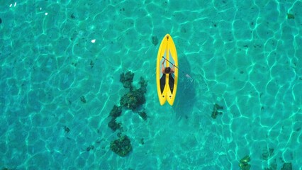 Aerial top down view woman paddle yellow sup. Crystal blue sea water coral reef. Outdoor active sport lifestyle travel on summer holiday vacation. Natural background. Drone shot