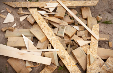Scraps of wooden boards in the form of pieces of different shapes lie in a pile after cutting during the construction of an ecological house.