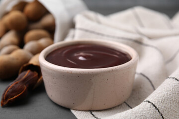 Bowl of tamarind sauce and fresh pods on table, closeup