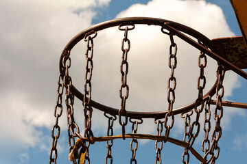 In a big city, between multi-story buildings, boys made a net for a basketball ring out of chain.