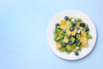 Plate of tasty fruit salad on light blue background, top view. Space for text