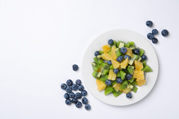 Plate of tasty fruit salad and blueberries on white background, flat lay. Space for text