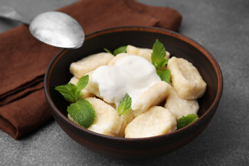 Bowl of tasty lazy dumplings with sour cream and mint leaves on brown table - obrazy, fototapety, plakaty
