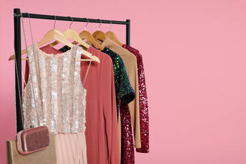Rack with stylish women's clothes on wooden hangers and accessories against pink background, space...