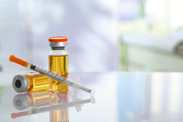 Glass vials and syringe with orange medication on white table. Space for text