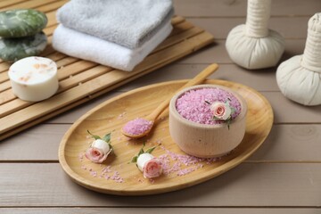 Fototapeta na wymiar Bowl of pink sea salt, roses, herbal massage bags and towels on wooden table