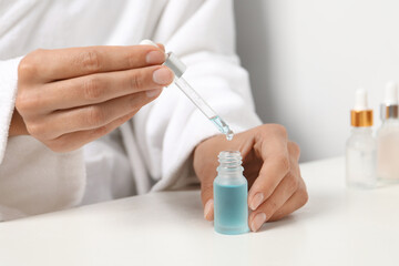 Woman with cosmetic serum at white table, closeup