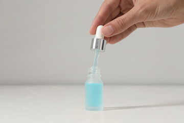 Woman with cosmetic serum at white table, closeup