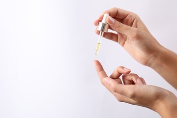 Woman applying cosmetic serum onto her finger on white background, closeup. Space for text