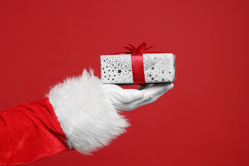 Santa Claus holding Christmas gift on red background, closeup