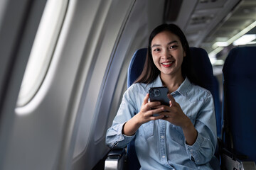 Asian people female person onboard, airplane window, using mobile and looking at camera while on the plane