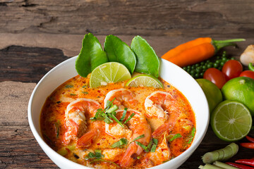 Tom Yum Goong or Shrimp soup spicy sour Soup Traditional food in Thailand contains chili, lime,lemongrass, lime leaf, along with cooked rice in a white dish on the old wood background.
