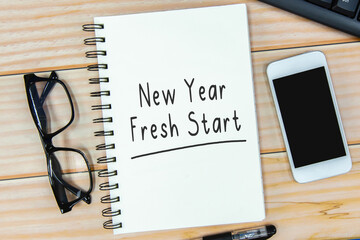 Open notebook with text “New Year Fresh Start” and eyeglass on wooden background.