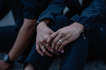 The couple held hands in a very romantic way, the woman's hand was wearing a wedding ring and white clothes while the man was wearing black clothes - obrazy, fototapety, plakaty