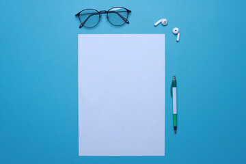 Glasses, air pods, pen and blank flyer poster to replace your design over blue background