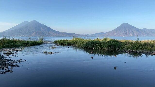 Sunrise HD video footage of dawn on Lake Atitlan Guatemala with volcanoes in the background and swarms of birds swooping the river