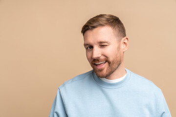 Flirting man winks look at camera, studio portrait isolated on beige. Bearded middle aged guy smiling winking playfully jokingly impishly with one eye, hinting, hidden intent, non-verbal communication - obrazy, fototapety, plakaty