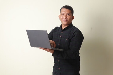 Asian mature man looking at the camera while holding a laptop and showing a very happy expression