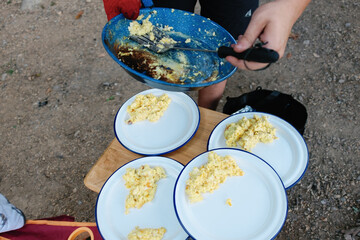 Scramble eggs being served off an enamel camping skillet and spatula onto plates. 