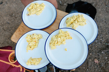 Scramble eggs on enamel plates at a campsite. 