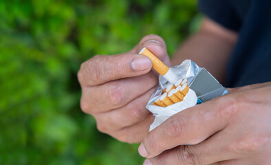 Close up man hand holding peel it off cigarette pack prepare smoking a cigarette over nature background.