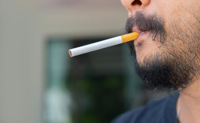 Close up of beared man smoking cigarette on balcony background.