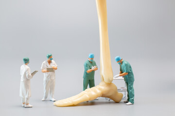Miniature people , Anatomy model of the human ankle joint with a doctor on a grey backdrop