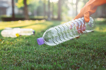 Volunteer woman hands wearing glove and keep plastic bottle from grass floor at public park,Dispose...