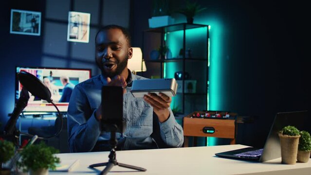 Content creator in studio films Bluetooth speaker video review for tech enthusiasts. African american viral online star hosts technology internet show, unboxing portable audio system