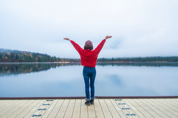 Tourist woman in red winter coat standing with hands raised, feeling free, Pyramid Lake pier,...