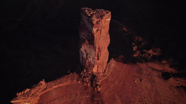 Aerial tilt retreats from shadow behind golden Castleton Tower, sunset