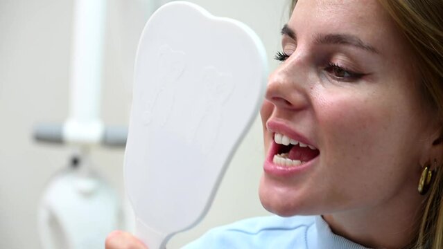 Young Beautiful woman smile after Dental Whitening process smile in mirror. Teeth whitening with UF Lamp, Led Lamp and gel in Dental Clinic. 4k 120 fps slow motion Raw footage
