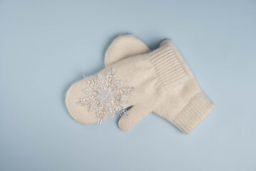 Warm white winter mittens with snowflake on blue background. Top view, flat lay.
