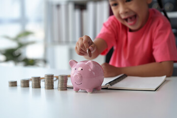 Cute little Asian girl playing with coins, making money in piles, putting money in a piggy bank....