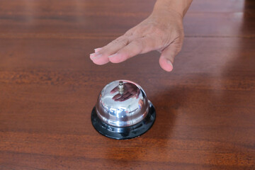Close up top view of a hand to press a service bell on a wooden desk calling for help