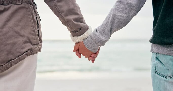 Back, beach and a parent holding hands with a kid while standing outdoor on sand by the coast. Family, children and people on holiday or vacation together during summer for travel and bonding closeup