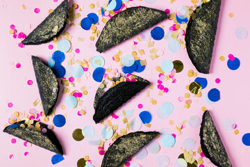 The photo shows a group of colorful confetti and taco against a pink pastel background.