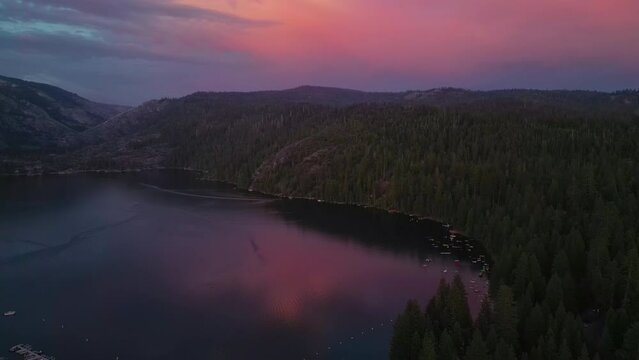 4k drone footage of a beautiful pink and purple sunset at Pinecrest lake in Pinecrest, California with the reflection in the water with boats. surrounded by pine trees