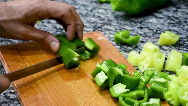 Close-up of a hand cutting green bell pepper on a chopping board in the kitchen.